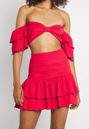 Mujer con un top corto rojo con los hombros descubiertos y mangas con volantes, combinado con una minifalda de cintura alta con volantes a juego.