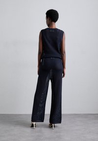 Navy strikket to-delt sett som inneholder en ermeløs topp og vide bukser. Stoffet har et teksturert mønster med åpne vevdetaljer og minimale sømmer.