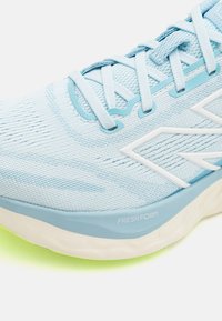 Lyseblå idrettssko med en teksturert mesh-overdel, kontrasterende hvite detaljer og en dempet såle merket "FRESH FOAM."
