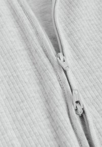 Giacchino grigio chiaro con zip prendisole, caratterizzato da una texture a costine e da una robusta cerniera con un tirante coordinato sulla parte anteriore.