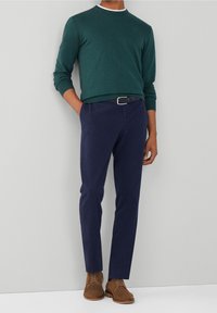 Pull vert foncé avec un col rond et des manches longues, pantalon bleu marine, et chaussures en daim marron. Design simple avec une texture lisse.