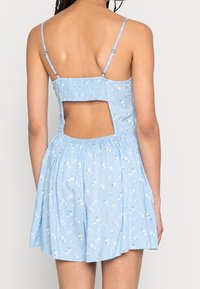 Světle modré šaty s květinovým vzorem, smyčkovaným zadním dílem, tenkými ramínky a otevřeným zádovým designem. Rozšířená sukně s jemnou texturou.