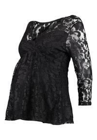 Haut de maternité en dentelle noire avec des manches longues, un buste ajusté et une coupe fluide. Motif floral sur l'ensemble, avec un col en scoop.