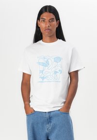 Tricou alb din bumbac cu un design abstract albastru, având textul "LIBERTATE ÎN FAța HAOSULUI," asortat cu pantaloni scurți din denim de un albastru deschis.