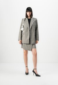 Grå rutete blazer med doble knapper, kombinert med et matchende rutete mini skjørt. Stylet med svarte spisse hæler og en liten hvit veske.