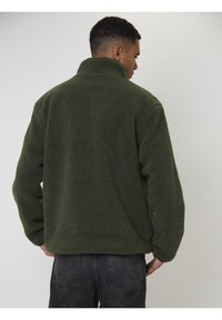 Giacca in fleece verde con colletto alto. Materiale morbido e testurizzato. Vestibilità rilassata, con spalle scese e orlo dritto.