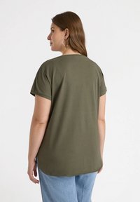 Olivengrön T-shirt med kort ärm, rund halsringning och avslappnad passform, med en böjd nederkant och mjuk tygstruktur.