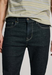 Tummat farkut slim fit -mallissa, joissa on kultaiset ompeluaksentit, yksi etutasku ja klassinen napp closure.