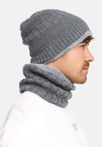 Bonnet gris en maille avec une texture côtelée et une doublure douce ressemblant à de la fourrure. Écharpe tour de cou gris assortie, présentant un motif de point froncé.