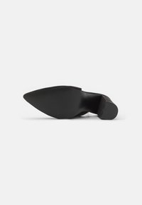 Escarpin noir à bout pointu avec une surface texturée et un talon fin. La semelle présente une texture à motif pour une meilleure adhérence.