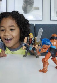 Action figures display vibrant colors: one with blonde hair, a silver sword, muscular build; another with blue accents; kids engage playfully.