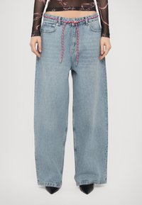 Helle blaue weite Jeans mit hoher Taille, ausgestattet mit einer rot-weißen geflochtenen Kordel und kontrastierenden schwarzen spitzen Schuhen.