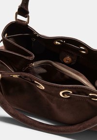 Sac à main en suède marron avec une texture douce, doté de quincaillerie dorée, d'une poche zippée intérieure et d'œillets métalliques pour la fermeture.