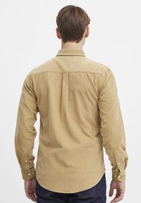 Beige corduroy overhemd met knopen, voorzien van een klassieke kraag, lange mouwen met knopenmanchetten en een achterkant met een plooi voor meer bewegingsvrijheid.