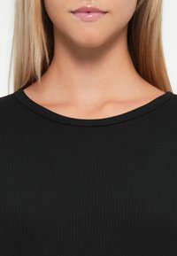 Haut noir côtelé avec un col arrondi. Le tissu semble lisse avec une texture délicate, soulignant le design ajusté.