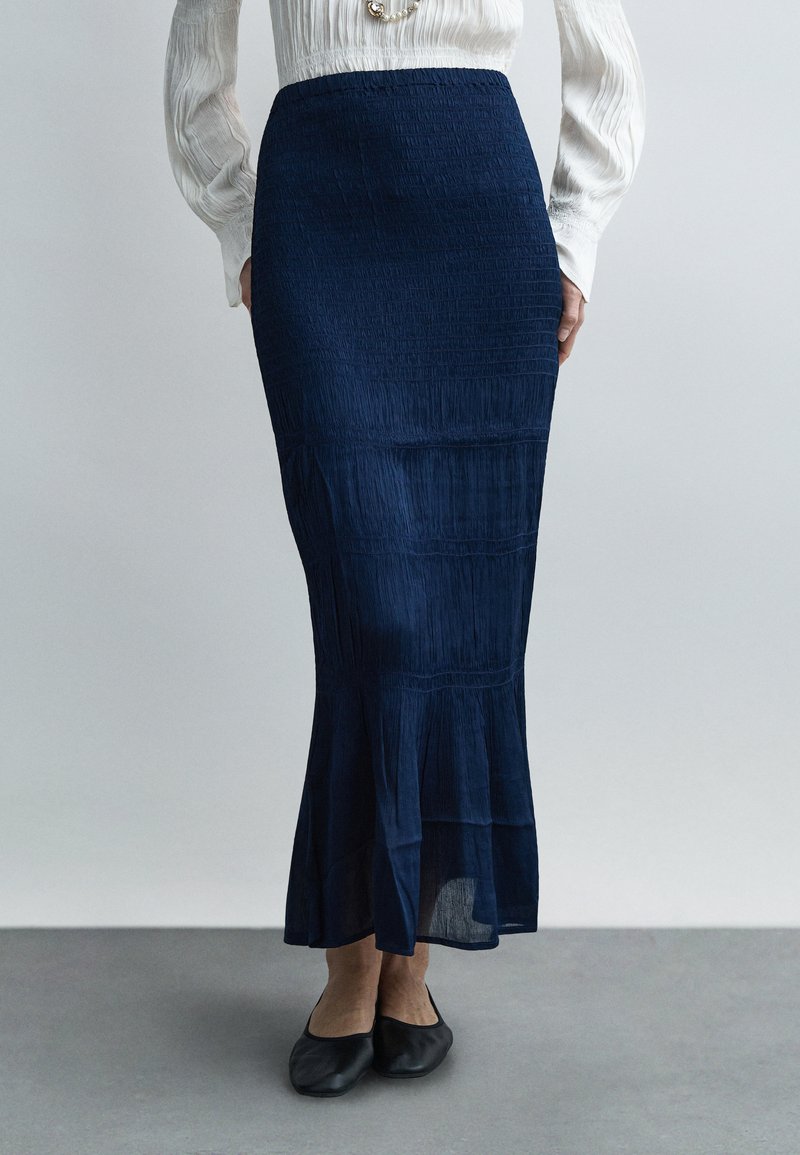 Tumesinine voltidega midi-seelik, millel on lõhenev ääreosa ja tekstureeritud kangas. Mustade ballerinate ja lihtsa, kuid elegantse disainiga komplekt.