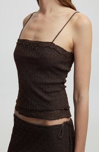 Top in maglia marrone con una texture, spalline sottili regolabili e bordi arricciati. Presenta un orlo multilivello e una gonna coordinata con motivi simili.