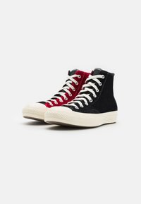 Sneaker alte con pannelli in suede nero e rosso, lacci bianchi e suole in gomma con dettagli testurizzati.
