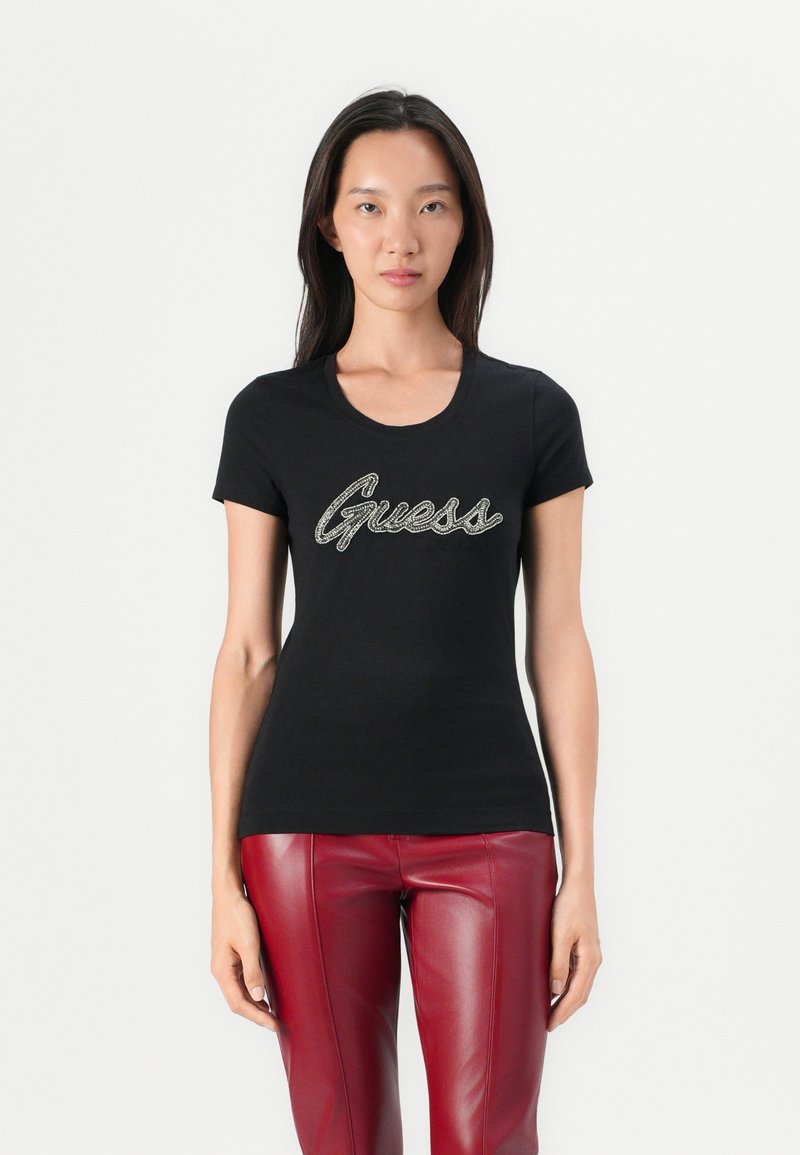 Must have musta T-särk, millel on ümar kaelus, esiküljel on "Guess" metallikult hõbedases kursiivis. Kombineeritud punaste kunstnahast pükstega.