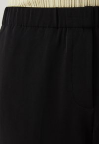 Pantalon en tissu noir avec une taille élastique, présentant une texture lisse, des poches latérales et un design décontracté.