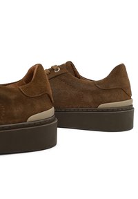 Scarpe in suede marrone con un design a profilo basso, suola in gomma, cuciture visibili e chiusura con lacci.