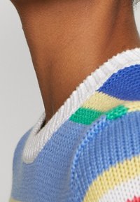 Närbild av en persons nacke och axel som bär en stickad tröja med vita, blå, gröna och gula mönster.