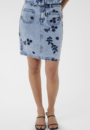 Hele sinine teksaseelik tume lillemustriga, ees taskud, kantud mustade rihmkinniste sandaalidega seisval inimesel.