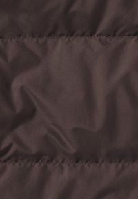 Tessuto marrone scuro con una consistenza liscia, caratterizzato da linee di cucitura visibili e una leggera lucentezza, creando un aspetto stratificato.