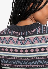 Suéter de punto con un diseño negro y estampado en rosa, azul y verde. Presenta un cuello redondo y una etiqueta con el logo de Quiksilver en la parte de atrás.