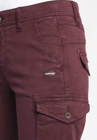 Burgundské cargo kalhoty z měkké látky s bočními kapsami, uzavřené knoflíkem s malou nášivkou loga.