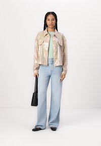 Sequin jacket with two front pockets in light beige, paired with a mint green top and high-waisted light blue jeans. Black handbag and shoes.