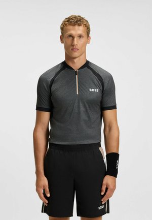 Kortärmad träningsskorta i mörkgrått med svarta detaljer, dragkedja i kragen och logotyp. Kombinerad med svarta shorts och ett matchande handledsband.