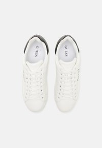 Sneakers bianchi in pelle liscia con dettagli neri sul tallone, design con lacci e logo sul lato. Stile minimalista e moderno.