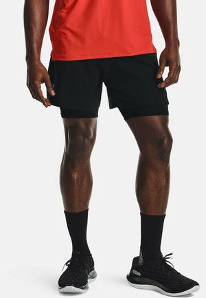 Beine und Oberkörper einer Person, die ein rotes Hemd, schwarze Sportshorts mit integrierten Kompressionsshorts, schwarze Crew-Socken und schwarze Laufschuhe trägt.