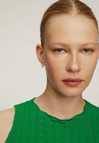 Top sin mangas de color verde texturizado con un escote redondeado, que presenta un sutil patrón arrugado, acompañado de pendientes de aro plateados.