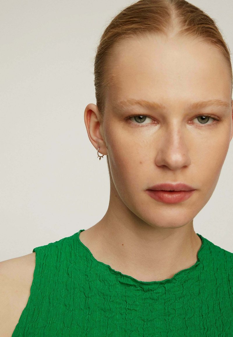 Top sin mangas de color verde texturizado con un escote redondeado, que presenta un sutil patrón arrugado, acompañado de pendientes de aro plateados.