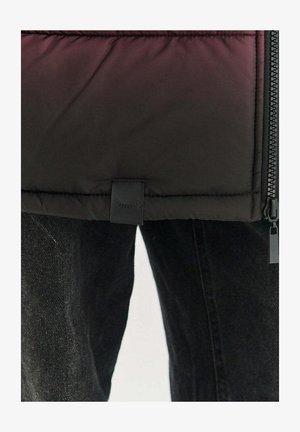 Kurtka puchowa, czarna z efektem gradientu. Posiada zamek błyskawiczny, detale przeszyć oraz małą materiałową metkę na dole. Połączona z szarymi jeansami.
