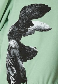 Žalias džemperis, kuriame pavaizduota juodai balta klasikinės statulos grafika su detaliais sparnais ir plazdančiais drabužiais.