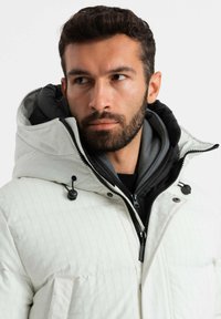 Cappotto bianco trapuntato con colletto alto e fodera nera, dotato di zip e chiusure a cordino, con dettagli delle tasche ben visibili.