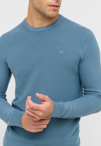 Maglione blu a collo rotondo lavorato a maglia con un tessuto testurizzato, maniche lunghe e un piccolo logo in mostra sul petto.