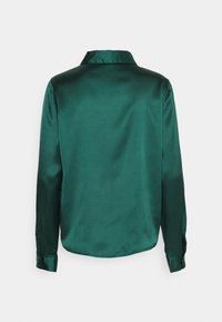 Chemise longue à manches longues en satin vert, avec un col en V, texture lisse et poignets boutonnés. La vue arrière montre un ourlet légèrement incurvé.