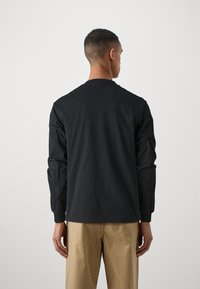 Black long-sleeve t-shirt featuring a round neckline and relaxed fit, made of cotton fabric, paired with light beige pants.