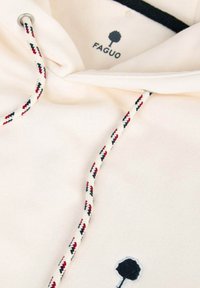 Sudadera color crema con cordones en rojo, negro y blanco, y un logo de árbol negro con el texto "FAGUO" en el pecho.