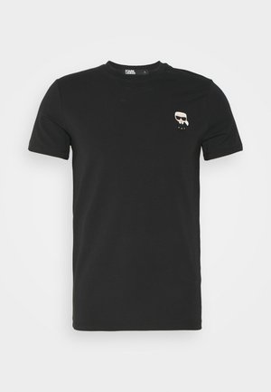 T-shirt nera in cotone con maniche corte, colletto rotondo e una piccola grafica a fumetto sul lato sinistro del petto, raffigurante un volto con occhiali.