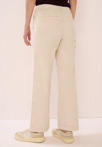Světle béžové široké kalhoty s elastickým pasem a zadními kapsami. Nosí se s béžovými teniskami s krémovými detaily. Hladká textura.
