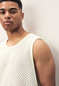 Canottiera leggera color crema in mesh con motivo geometrico e scollo rotondo, che valorizza spalle e braccia.