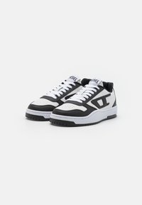 Baskets de sport noir et blanc avec un bout perforé, lacets blancs, logo proéminent et semelle en caoutchouc texturée. Matériaux en cuir lisse et tissu.