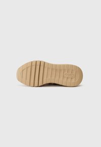 Semelle en caoutchouc beige avec surface texturée, ornée de rainures horizontales et d'un logo circulaire. Design épuré et minimaliste sans motifs visibles.