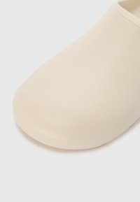 Beige clogs with a smooth, matte finish. Rounded toe and seamless design, made from durable synthetic material. No visible hardware or patterns.