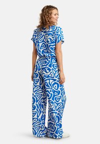 Zweiteiliges Outfit mit einem blau-weißen abstrakten Muster. Das locker sitzende Oberteil hat kurze Ärmel und wird mit weiten Hosen im gleichen Design kombiniert.